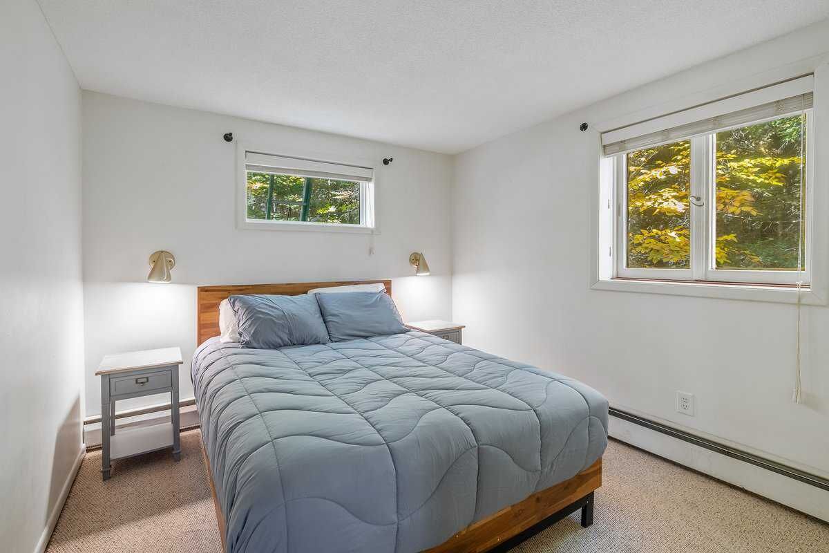 A bedroom with a bed, two bedside tables, a window with a view of trees, and a small window above the bed.