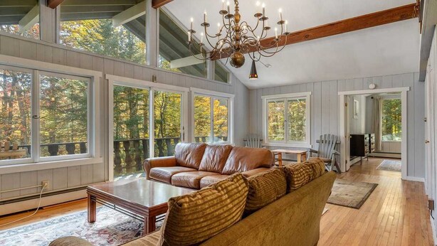 A spacious living room with large windows, a chandelier, and a wooden floor. - Spacious Stratton Mountain Home  - Perfect for families! (Winhall)