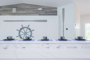 A kitchen with a white countertop, a wooden ceiling, and a wall-mounted ship's wheel.
