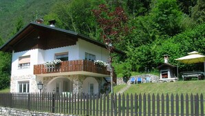 Eine zweigeschossige Chalet mit Naturstein-Fassade, Holzbalkon mit Blumenkästen und einer Steinmauer mit einem Pfostenzaun davor.