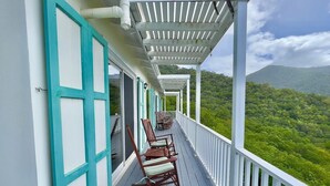 A covered porch with wooden chairs, white railings, and a view of a lush green landscape. - Quiet hillside villa with expansive sea, beach, and mountain views... (St Croix)