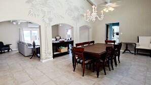 Een ruime woonkamer met een eettafel, stoelen en een bank. Achterin is een keuken te zien.