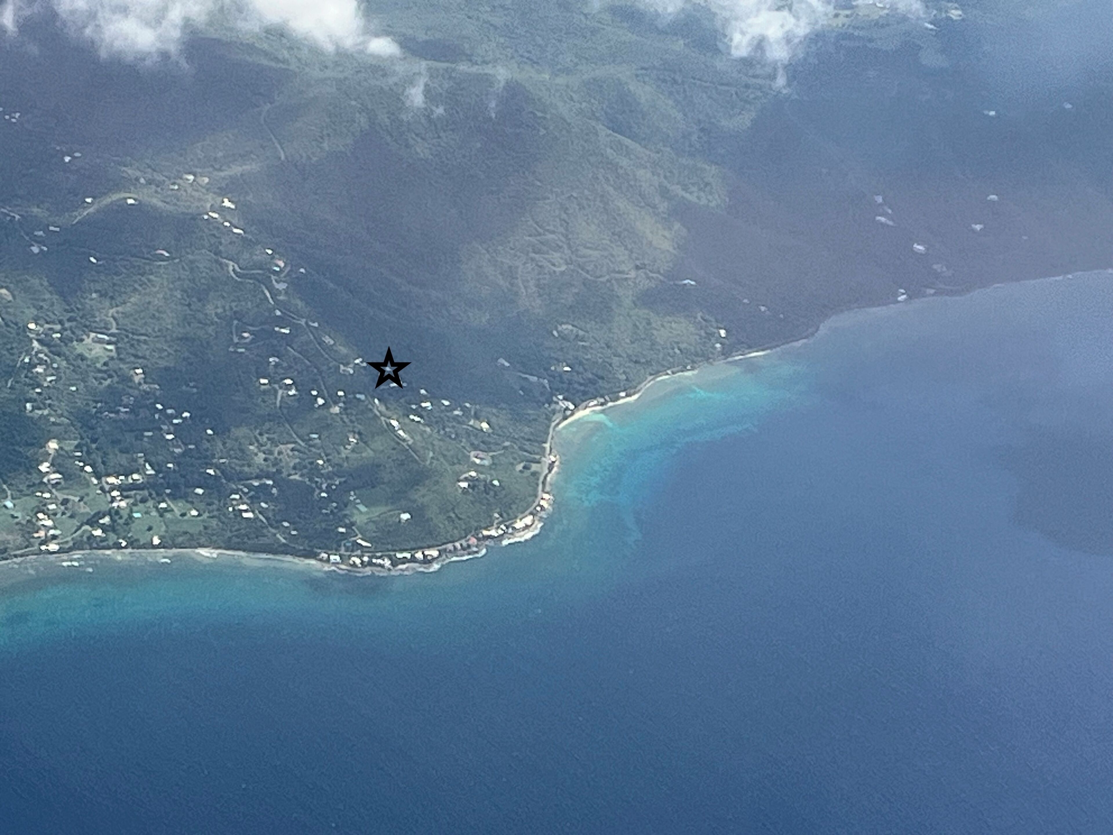 Vue aérienne d’une zone côtière avec une petite île, des eaux d’un bleu limpide et un symbole en forme d’étoile indiquant un emplacement.