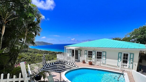 A pool area with a view of the ocean, a white building with a turquoise roof, and a white picket fence. - Quiet hillside villa with expansive sea, beach, and mountain views... (St Croix)