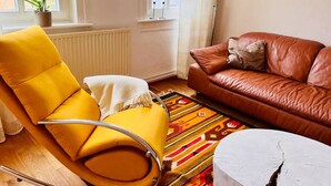 Ein Wohnzimmer mit einem gelben Sessel, einem braunen Ledersofa, einem gemusterten Teppich und einem weißen Beistelltisch.