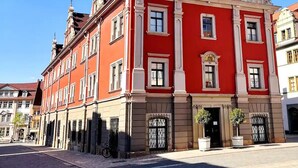 Ein rotes Gebäude mit einem Glockenturm, großen Fenstern und einem zentralen Eingang.