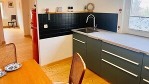 Eine kompakte Küche mit schwarzem Fliesenspiegel, einem Spülbecken und einem Fenster.