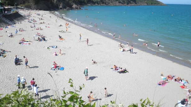 A beach with people sunbathing and swimming.
