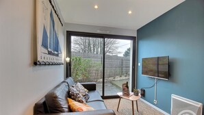 A modern living room with a leather sofa, a small table, a mounted TV, and a large sliding glass door leading to an outdoor area.