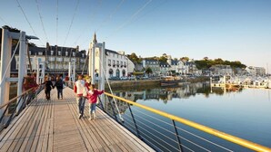 A wooden pedestrian bridge over calm water with buildings and a marina in the background.