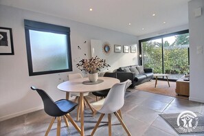 A modern living room with a dining area, large windows, and a view of greenery.