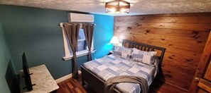 Ein Schlafzimmer mit einem hölzernen Kopfteil, einem Bett mit einem gemusterten Bettbezug, einem Nachttisch mit einer Lampe und einem Fenster mit Vorhängen.