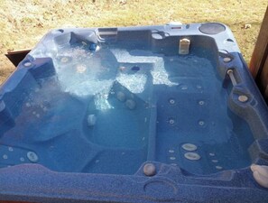 Ein Whirlpool mit klarer Glasabdeckung, zahlreichen Düsen und einer ihn umgebenden Holzterrasse.