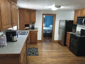 Kitchen area with a stove, microwave, coffee maker, and kettle, leading to a bedroom.