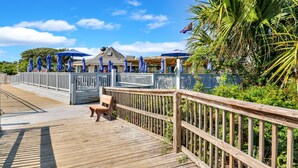Un muelle de madera con un banco, sombrillas azules y un edificio con tejado inclinado.