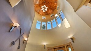 Ein Zimmer mit hohen Decken, Holzboden, mehreren Fenstern und Wandleuchten.