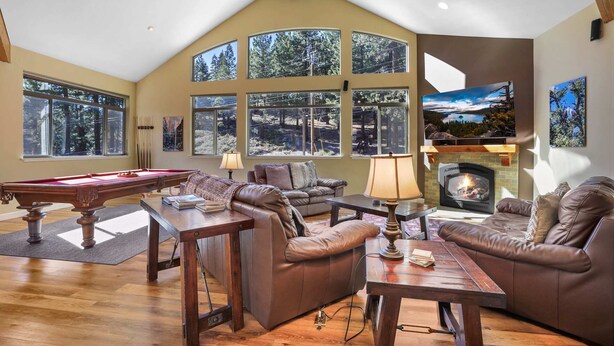 Ein geräumiges Wohnzimmer mit Billardtisch, Ledersofas, Kamin und großen Fenstern mit Blick auf einen Wald.