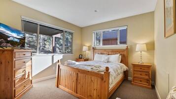 A bedroom with a wooden bed, two bedside tables, a dresser, and a TV on a stand.