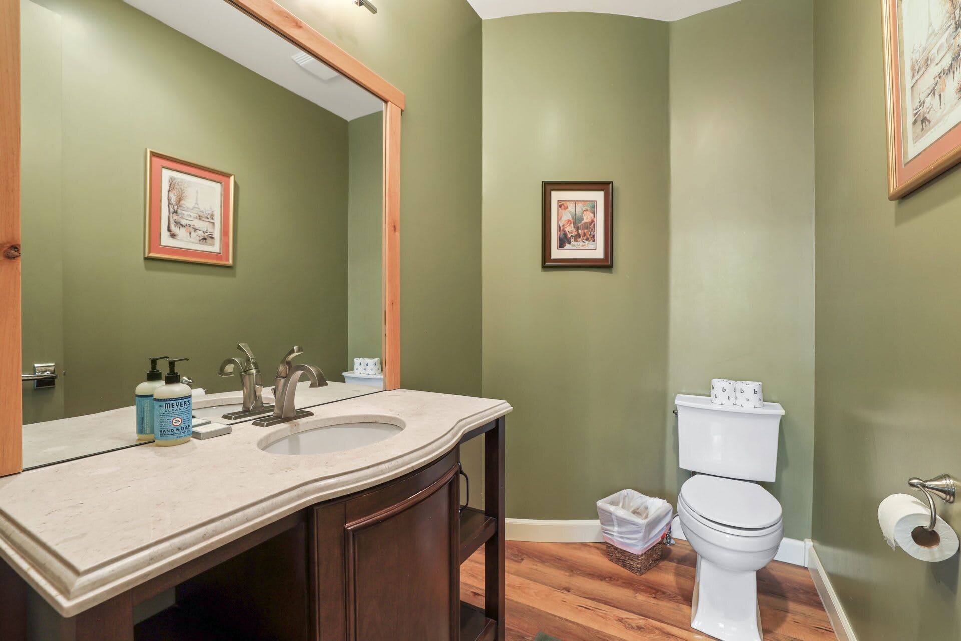 A bathroom with a vanity, two sinks, a toilet, and two framed pictures on the walls.