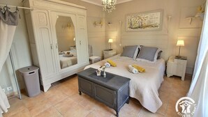A bedroom with a bed, nightstands, a dresser, a mirror, a chandelier, and a painting on the wall.