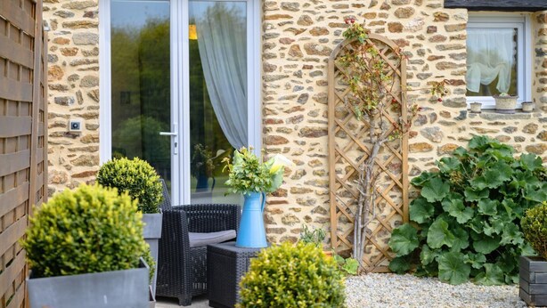 A stone building with a glass door, a small outdoor seating area with wicker furniture, and potted plants.