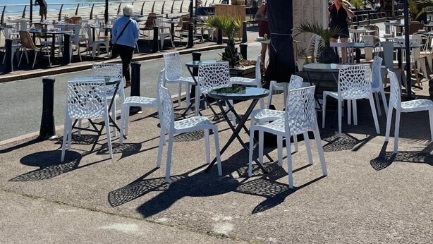 An outdoor café with white chairs and tables, umbrellas, and a view of the beach and sea. - Trestraou - Perros Guirec (PERROS GUIREC)