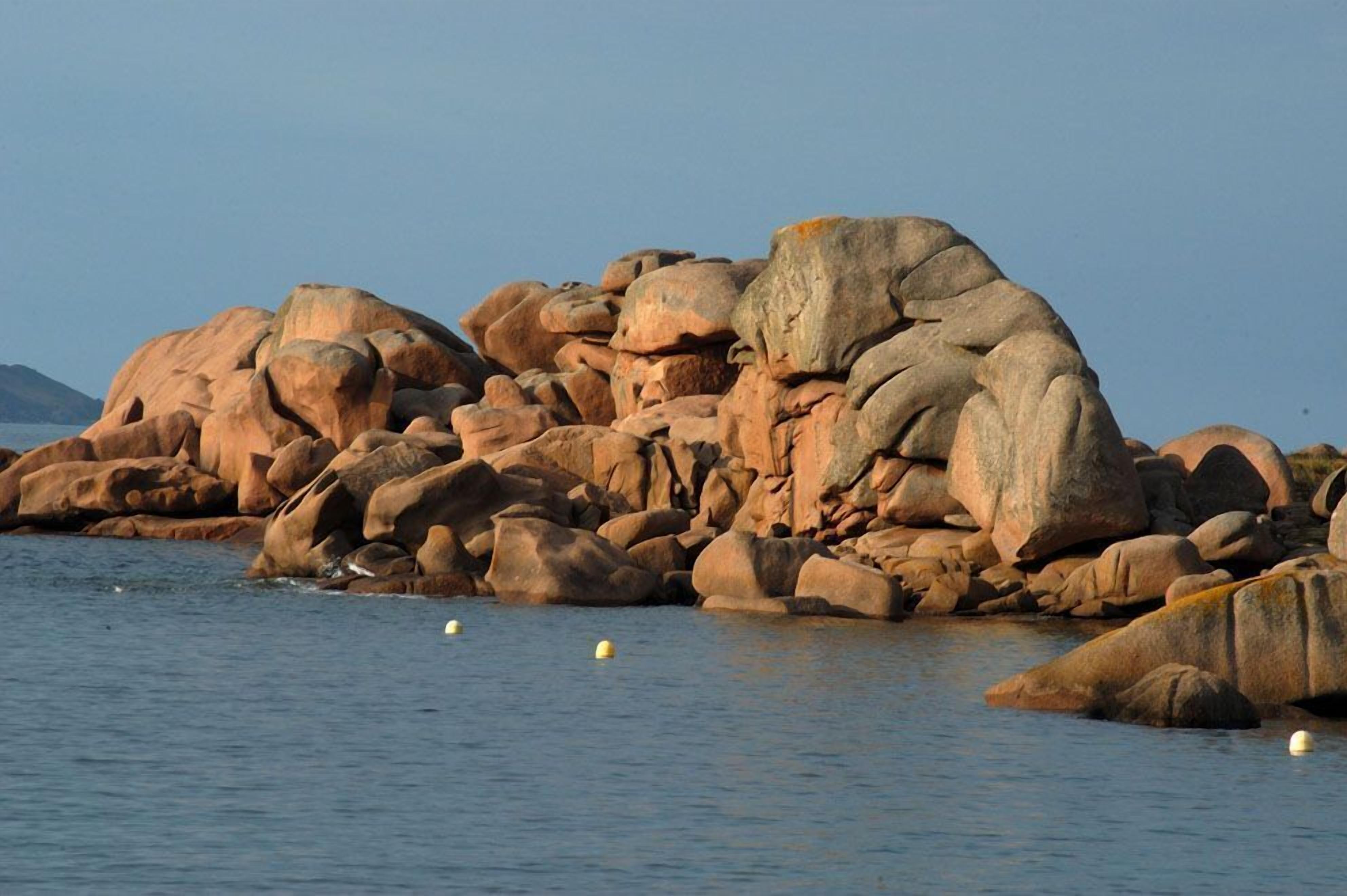 Une côte rocheuse parsemée de gros blocs et bordée d’une eau calme.