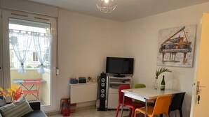 Un espacio habitable compacto con un sofá, una mesa de comedor con sillas, un televisor y una alfombra colorida.