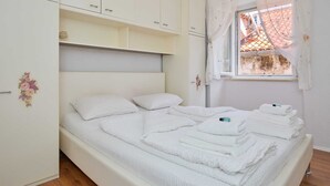 A bedroom with a bed, white curtains, and a window with a view of buildings.