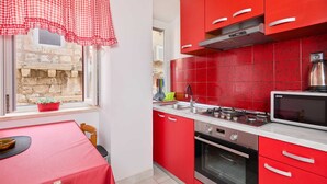 A compact kitchen with red cabinets, a gas stove, a microwave, and a window with a view of a stone wall.