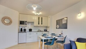 A compact kitchen with white cabinets, a microwave, and a dining area with a table and chairs. - Vue sur la Station - Erquy (ERQUY)