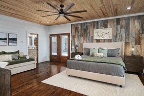 A bedroom with a wooden ceiling, a bed with a grey and green bedspread, a white bedside table, and a wooden wall panel. -  "LAKEVIEW": No Steps, HOT TUB, Boat/Swim Dock, Elevator (Arley)