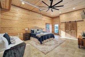 A spacious bedroom with a large bed, a ceiling fan, and wooden walls.