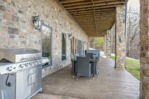 Une terrasse extérieure avec un mur en pierre, un barbecue et des meubles en osier.