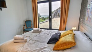 A hotel room with a bed, a chair, a window with curtains, and a view of the sea. - La Roche Mignonne - Trebeurden (TREBEURDEN)