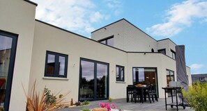 Una casa moderna con ampie finestre, un patio con tavolo e sedie e un giardino con rocce e piante.