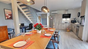 A modern kitchen with a dining area, featuring a wooden table set for four, a staircase, and a flat-screen TV mounted above the counter. - La Roche Mignonne - Trebeurden (TREBEURDEN)