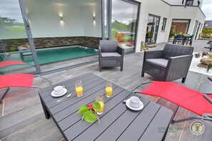 A modern outdoor dining area with a pool, wicker furniture, and a view of the surrounding landscape. - La Roche Mignonne - Trebeurden (TREBEURDEN)