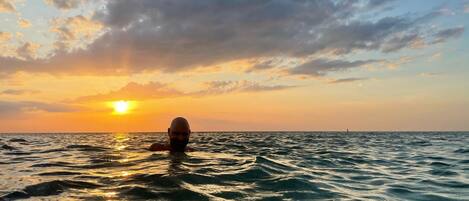 Iemand zwemt in de oceaan tijdens de zonsondergang.