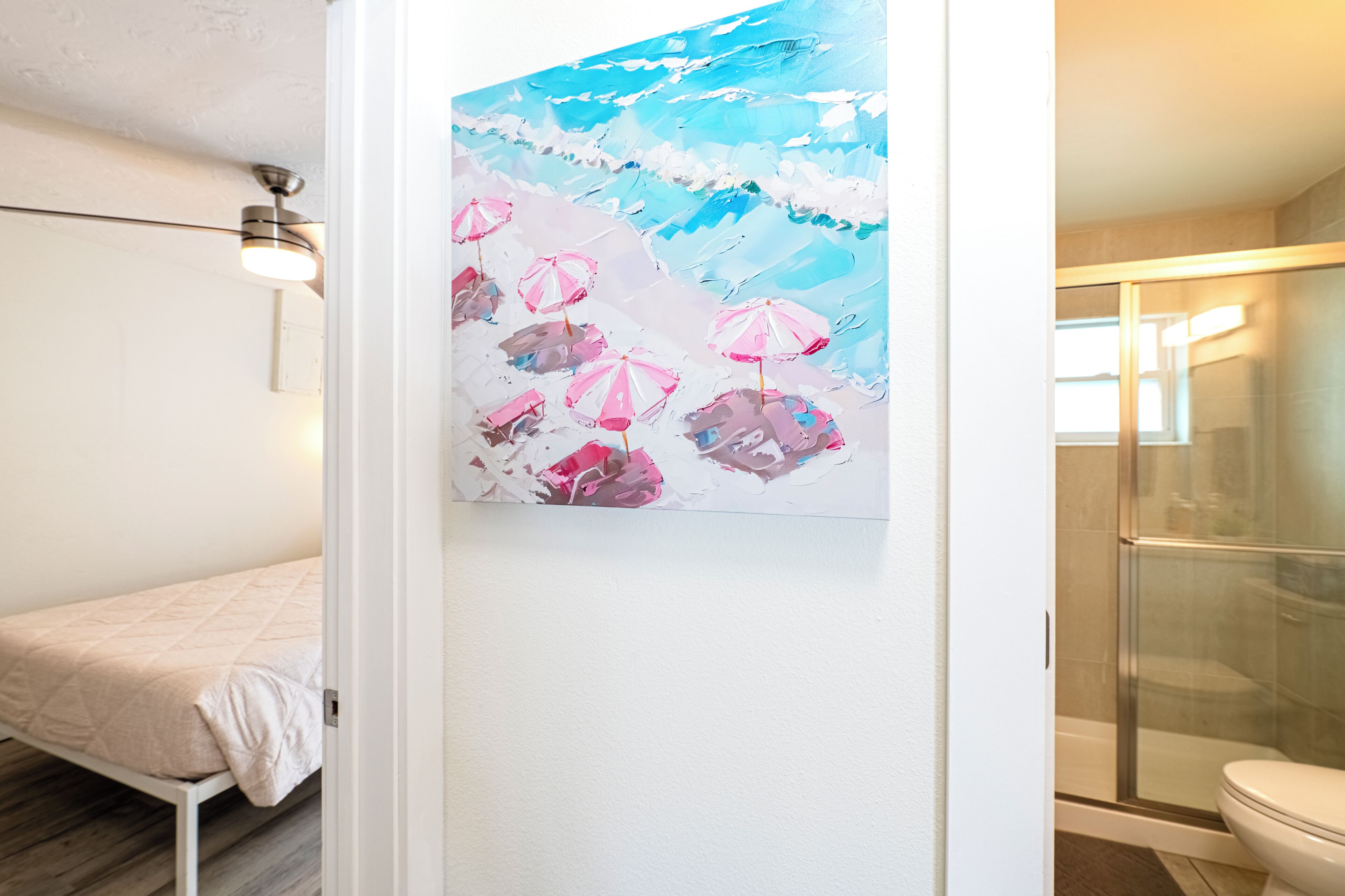 A bathroom with a glass shower enclosure, a white toilet, and a painting of pink umbrellas on the wall.