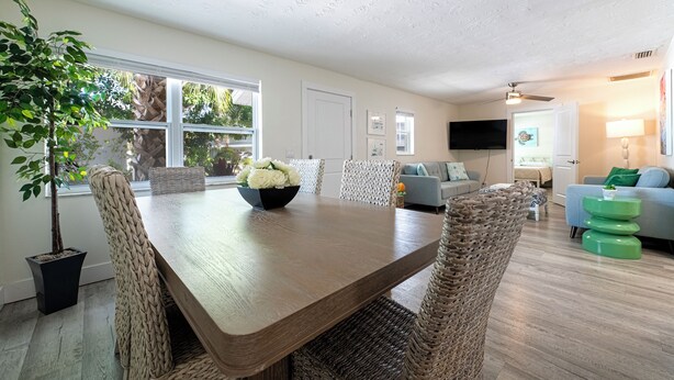 A dining area with a wooden table and woven chairs, a potted plant, and a bowl of flowers. - Family-friendly 2-bed, 2-bath ground-floor unit in Indian Rocks Beach. Sleeps eight with full kitchen, WiFi, smart TV, beach gear, and direct pool access. A comfortable, convenient base for sand days, sunsets, and easy coastal living (Indian Rocks Beach)