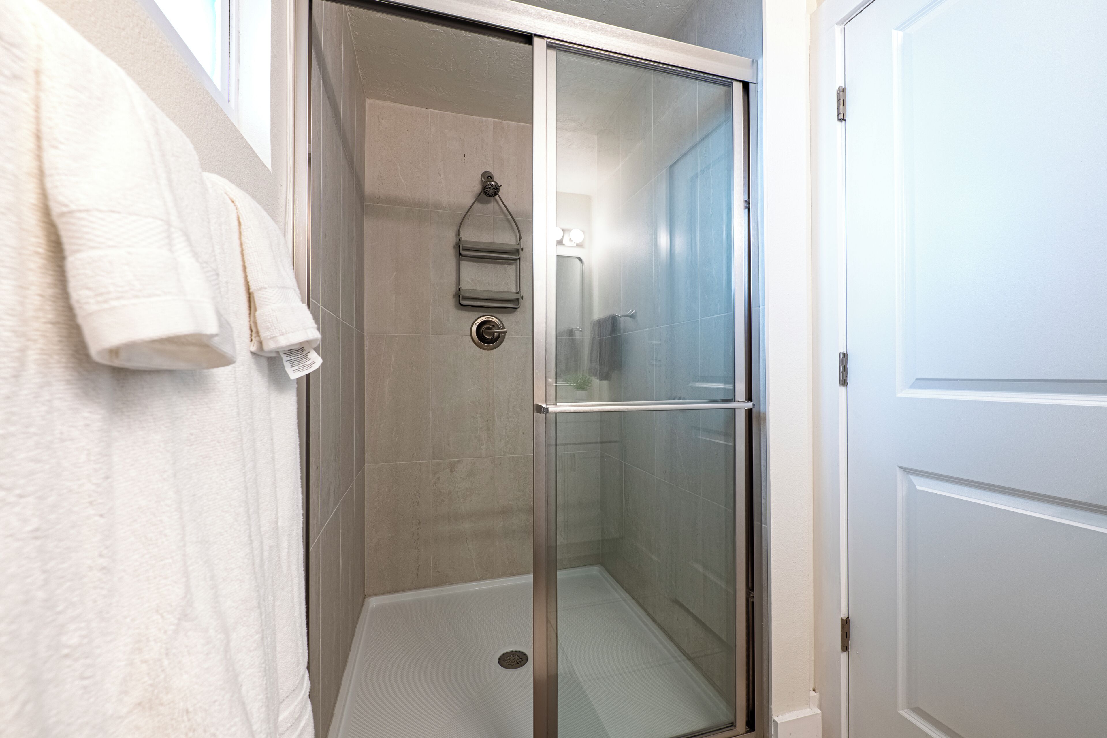 A walk-in shower with a glass door, a towel rack with towels, and a light switch on the wall.