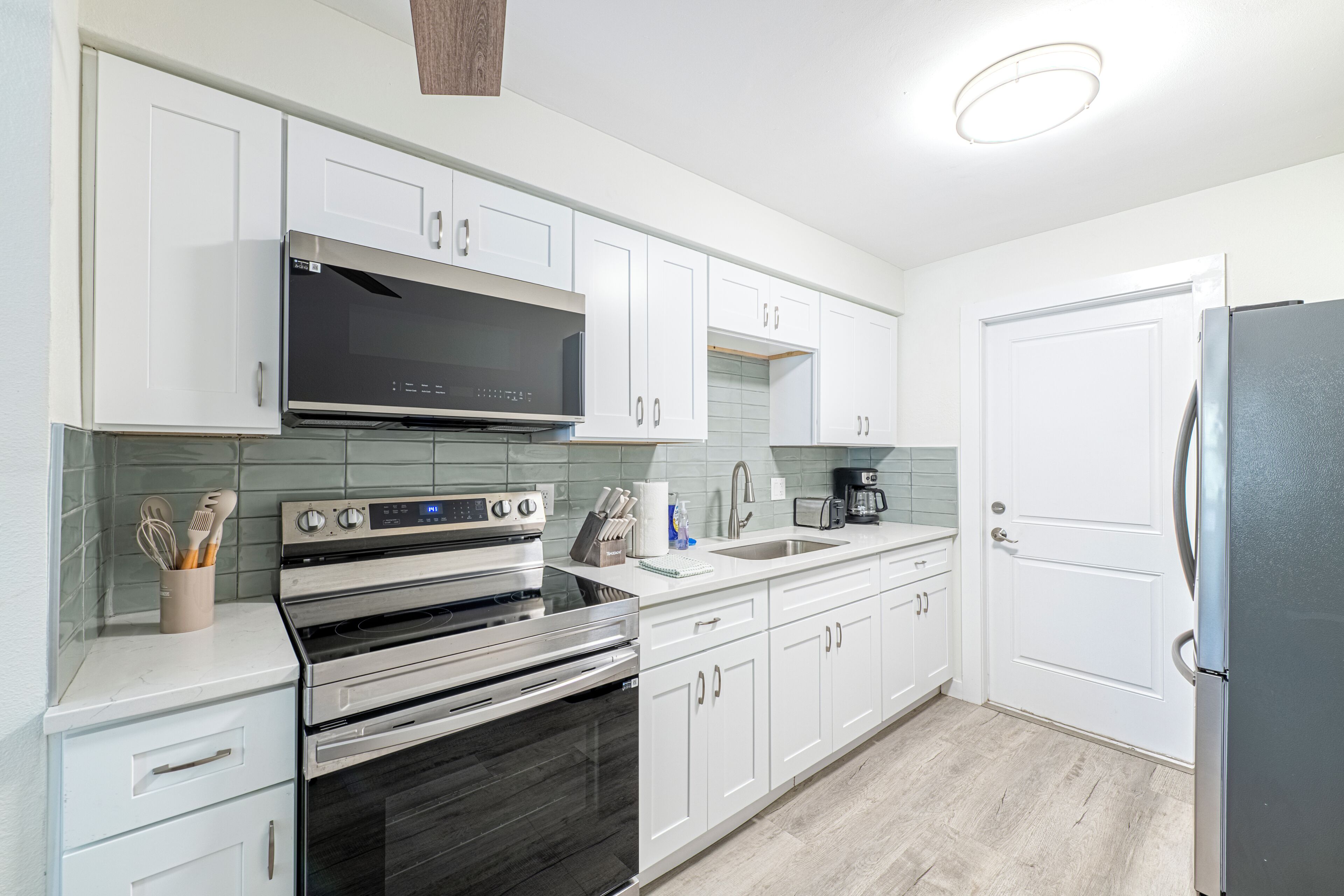 A modern kitchen with white cabinets, stainless steel appliances, and a tiled backsplash.