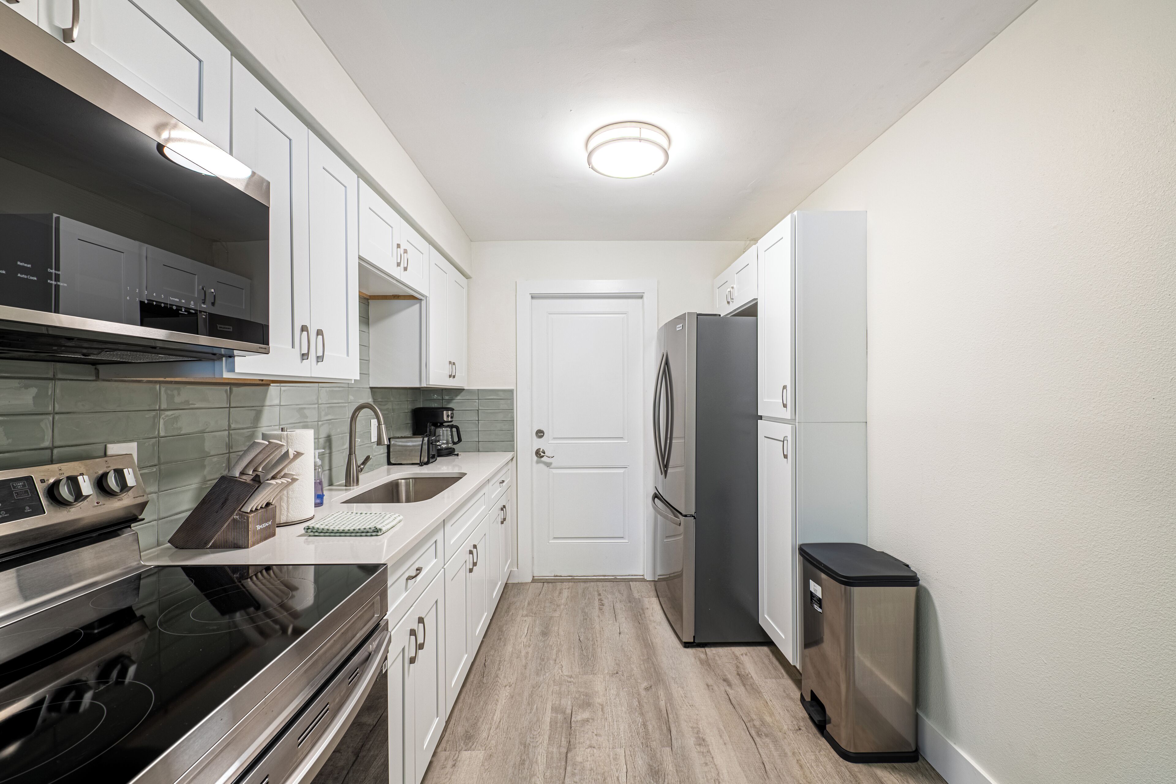 A compact kitchen with white cabinets, stainless steel appliances, and a tiled backsplash.