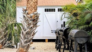 Patio con una parrilla, un cobertizo blanco y una palmera.