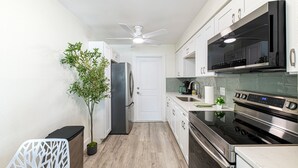 Una cocina moderna con armarios blancos, electrodomésticos de acero inoxidable, un ventilador de techo y una planta en maceta.