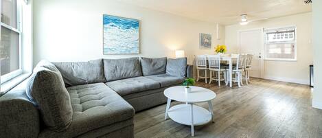 Una sala de estar moderna con un sofá modular, una mesita de centro redonda y un comedor con mesa y sillas.