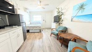 A compact hotel room with a bed, kitchenette, seating area, and a painting of a beach. - MySunsetView 6 Unit 4 Studio w kitchenette (Indian Rocks Beach)