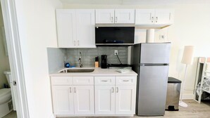 A compact kitchen with white cabinets, a stainless steel refrigerator, a microwave, and a sink. - MySunsetView 6 Unit 4 Studio w kitchenette (Indian Rocks Beach)