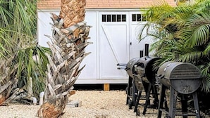 A backyard with a barbecue grill, a white shed, and a palm tree. - MySunsetView 6 Unit 4 Studio w kitchenette (Indian Rocks Beach)